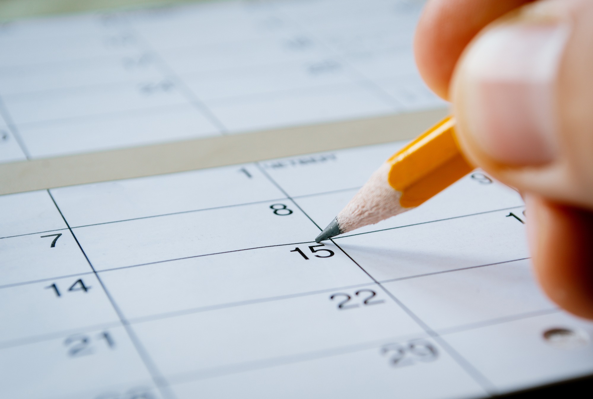 Person marking the date of the 15th with a pencil on a blank calendar with date squares as a reminder of an important day or to schedule a meeting or event