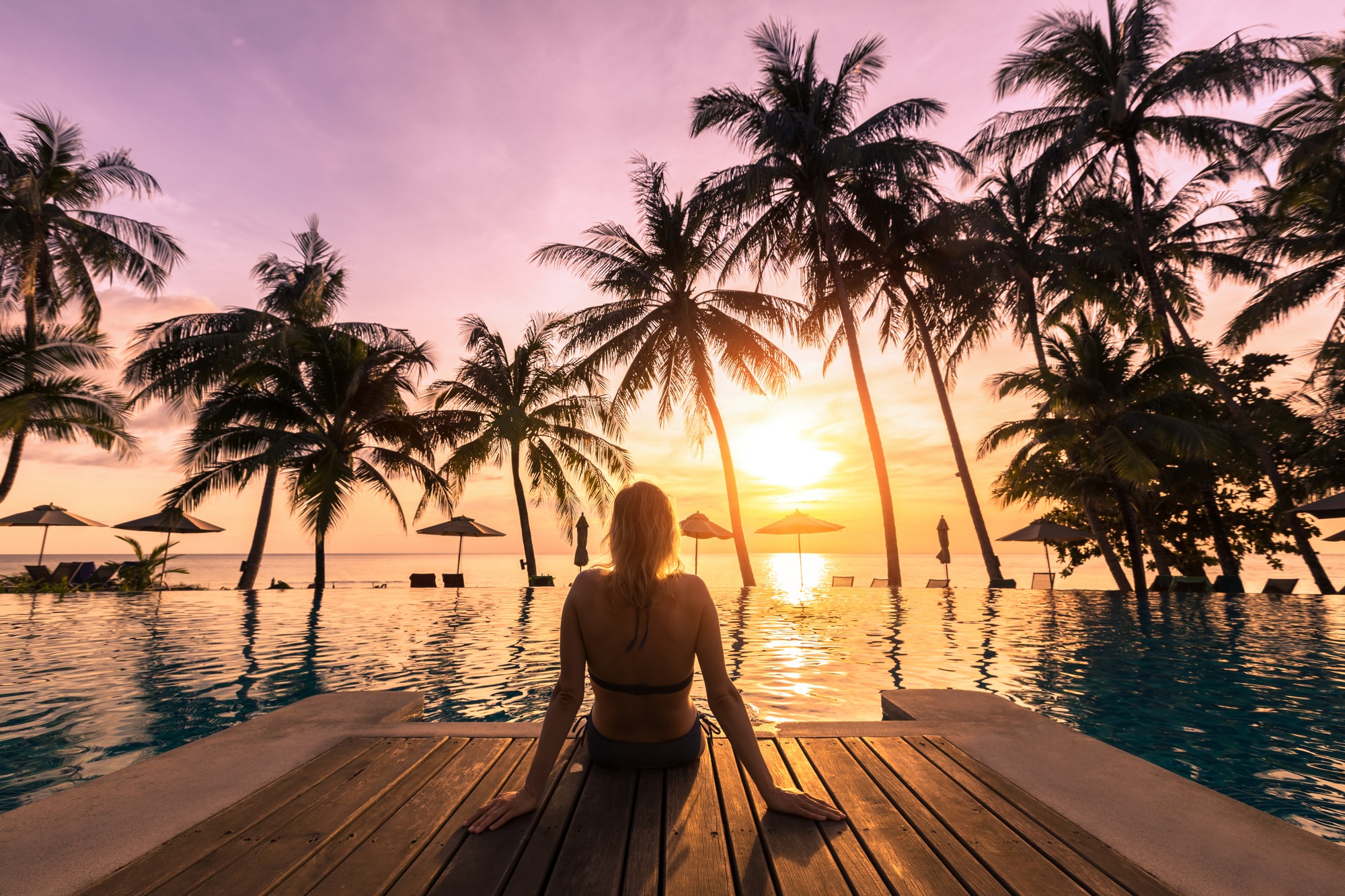 Woman relaxing by the pool in a luxurious beachfront hotel resort at sunset enjoying perfect beach holiday vacation